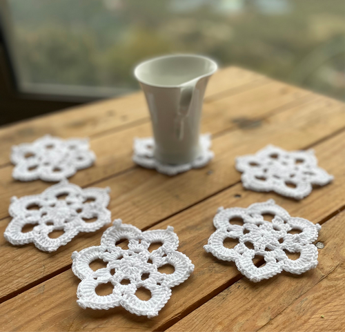 Set of white crocheted coasters on a wooden surface with a blurred natural background