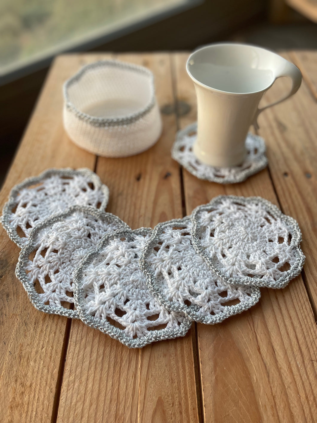 Set of crocheted coasters on a wooden surface with a cup and small basket.