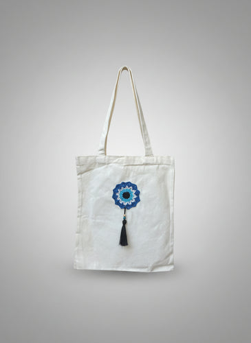 White tote bag with blue floral design and tassel on a wooden chair
