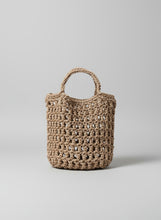 Load image into Gallery viewer, Brown woven handbag leaning against a light-colored wall with shadows cast by leaves.

