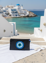 Load image into Gallery viewer, Black canvas pouch with blue hamsa evil eye at Greek beach
